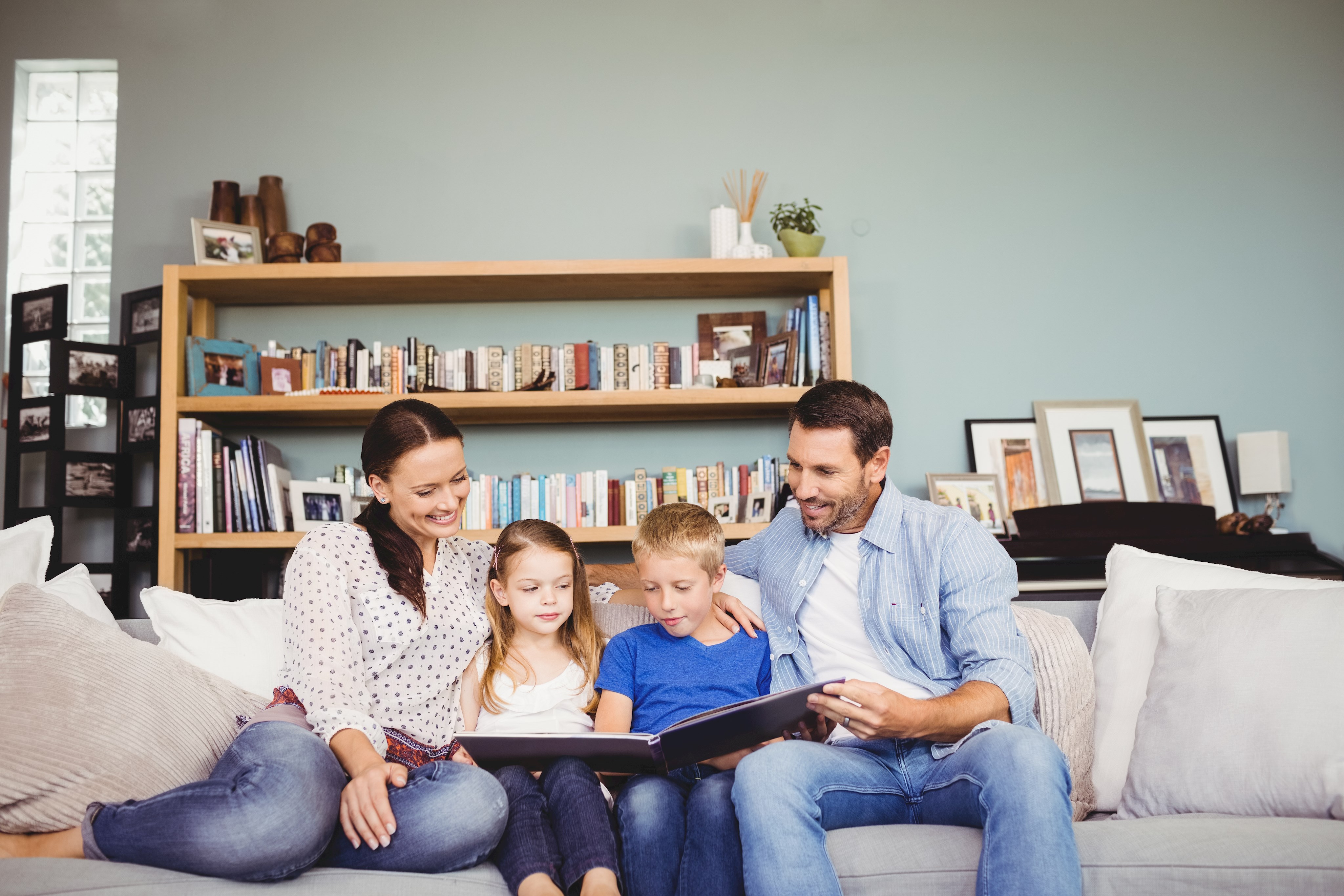 Mutter, Vater und zwei Kinder sitzen auf einem Sofa und lesen in einem Buch.